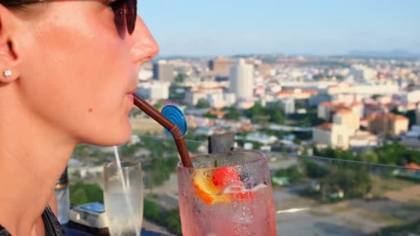 Vrouw die een sinaasappel cocktail drinkt van een rietje in een café op het dak op een hoogbouw, close-up — Stockvideo