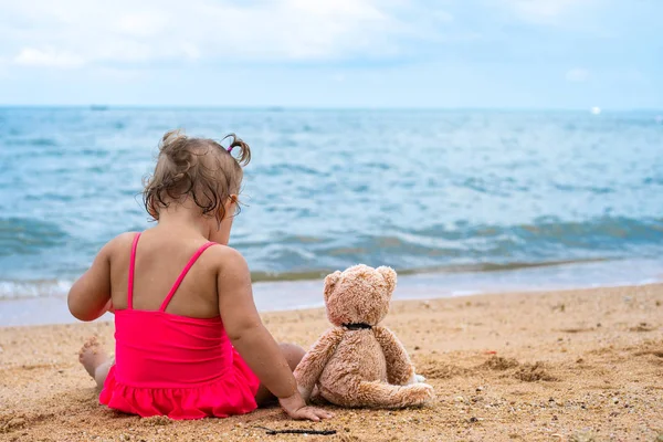 Милая девушка у моря. Молодая девушка с плюшевым мишкой сидит на пляже . — стоковое фото