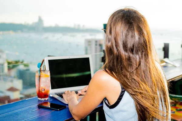 Жінка працює на ноутбуці в кафе на даху висотного зросту з красивим панорамним видом на місто, крупним планом — стокове фото