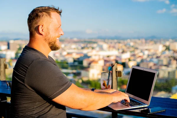 Чоловік працює на ноутбуці в кафе на даху з красивим панорамним видом. чоловік п'є коктейль і працює на комп'ютері . — стокове фото