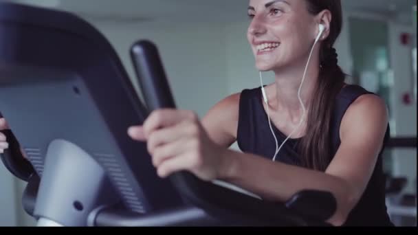 Ejercicio de entrenamiento cardiovascular en bicicleta en el gimnasio de fitness de la mujer que toma la pérdida de peso. femenino escucha música en los auriculares. Atleta músculo constructor estilo de vida . — Vídeos de Stock