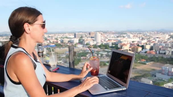 Kadın şehrin güzel bir panoramik görünümü ile yüksek katlı çatısında bir kafede bir dizüstü bilgisayar üzerinde çalışır, yakın — Stok video
