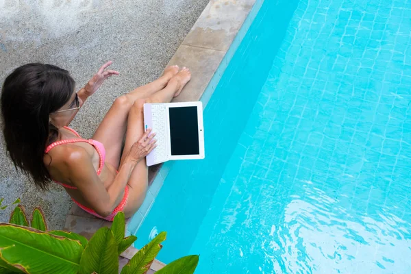 Жіночий фрілансер сидить біля басейну і працює на ноутбуці і кидає ноутбук у воду. Зайнятий під час канікул. Поняття віддаленої роботи. вибірковий фокус — стокове фото