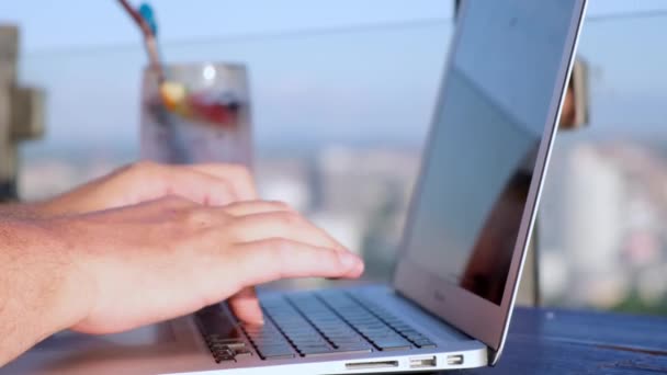 Masculino digitando em um laptop em um café no telhado de um arranha-céus com uma bela vista panorâmica da cidade, close up — Vídeo de Stock