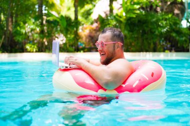 pembe gözlük pembe şişme daire içinde gülen Şişman komik adam bir yüzme havuzunda bir dizüstü bilgisayar üzerinde çalışır