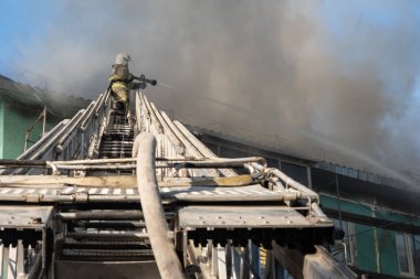 Merdivenlerdeki itfaiyeciler, yüksek katlı bir binanın çatısında çıkan yangını söndürüyor. üst görünüm