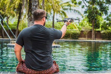 Sempatik bir adam uçuş için bir drone başlattı, hangi ile fotoğraf ve video çekebilirsiniz, yüzme havuzu yakınında, geri görünüm.