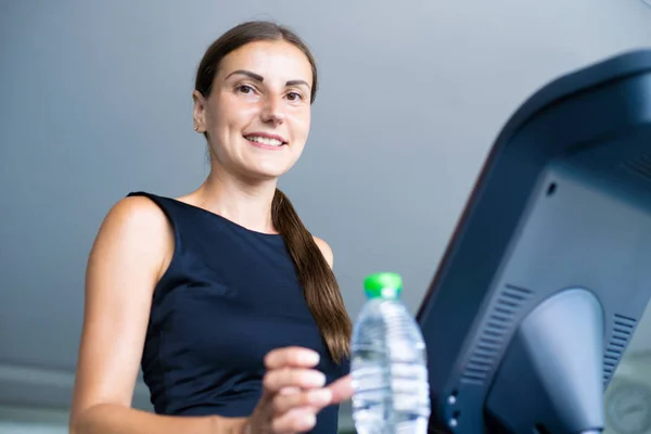 Smiling athletic woman drinking water on a treadmill. — Stock Photo, Image