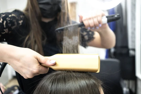 Cute girl with long brunette hair hairdresser doing hair lamination in a beauty salon. concept of hair care treatment, steam from hair — Stock Photo, Image