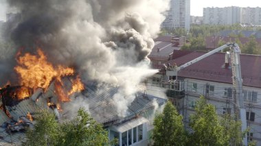 Yüksek katlı bir binanın yanan çatısı, yangından duman bulutları. İtfaiyeciler yangını söndürdü. üst görünüm