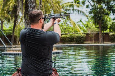 Sempatik bir adam uçuş için bir drone başlattı, hangi ile fotoğraf ve video çekebilirsiniz, yüzme havuzu yakınında, geri görünüm.