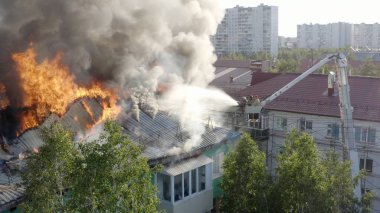 Yüksek katlı bir binanın yanan çatısı, yangından duman bulutları. İtfaiyeciler yangını söndürdü. üst görünüm