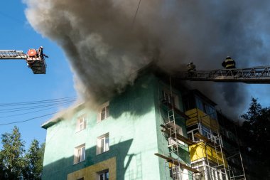 Merdivenlerdeki itfaiyeciler, yüksek katlı bir binanın çatısında çıkan yangını söndürüyor. üst görünüm