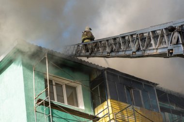 Merdivenlerdeki itfaiyeciler, yüksek katlı bir binanın çatısında çıkan yangını söndürüyor. üst görünüm