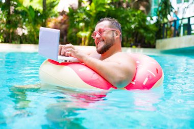 pembe gözlük pembe şişme daire içinde gülen Şişman komik adam bir yüzme havuzunda bir dizüstü bilgisayar üzerinde çalışır