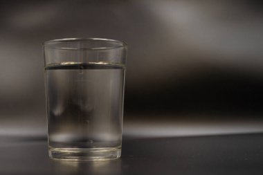 Sadece bir bardak su koyu ahşap bir masa üzerinde. Siyah bir zemin üzerine bir bardak maden suyu. Bir bardak su ile