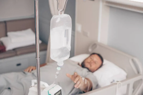 男性躺在医院的病床上。在医院里,一个人手的滴滴器. — 图库照片