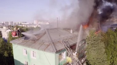 Merdivenlerdeki itfaiyeciler, yüksek katlı bir binanın çatısında çıkan yangını söndürüyor. üst görünüm