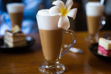 Latte bir cam kupa bir plumeria çiçek ile ahşap bir masa üzerinde duruyor