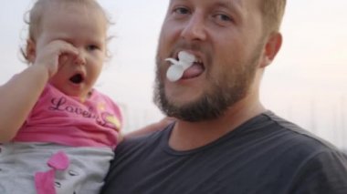 Baba kollarında küçük kızı ağlıyor, baba çocuğu neşelendirmek için çalışır ve bir çiçek, şaka, yavaş hareket, 4k.