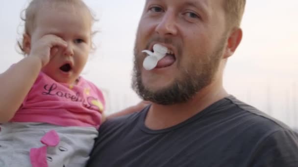 La pequeña hija en los brazos del padre llora, el padre trata de animar al niño y hay una flor, broma, cámara lenta, 4k . — Vídeos de Stock