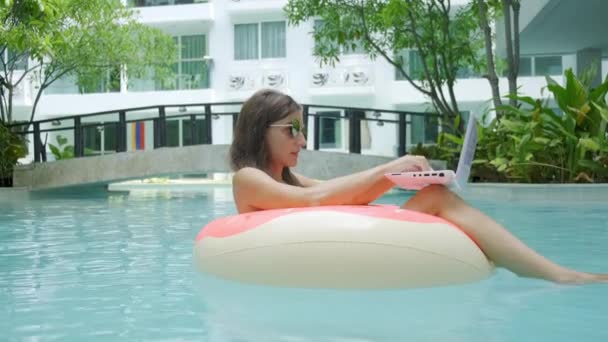 Vrouwelijke freelancer zit in een opblaasbare cirkel in het zwembad en gooit de laptop in het water. Druk tijdens de feestdagen. Het concept van extern werk. selectieve focus — Stockvideo