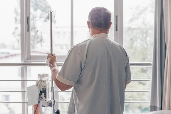 一个男人站在医院的病房里,向窗外望去。在医院里,一个人手的滴滴器. — 图库照片