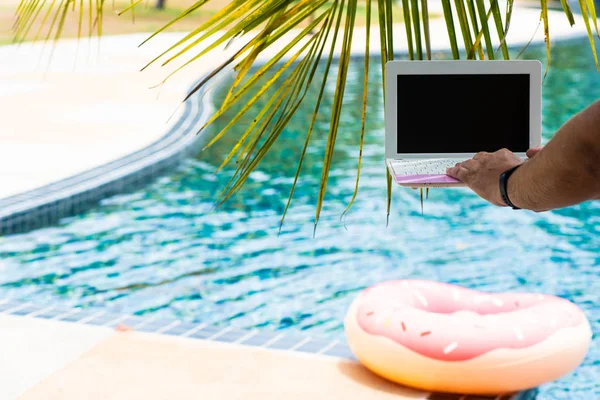 Чоловік працює на ноутбуці, сидячи біля басейну. Чоловічі руки на клавіатурі в басейні — стокове фото