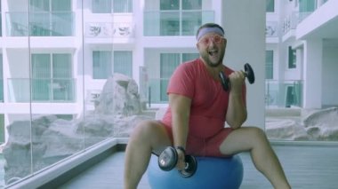 Pembe gözlük ve pembe bir tişört komik şişman erkek bir kız tasvir spor salonunda bir Fit Top Dambıl ile uğraşan