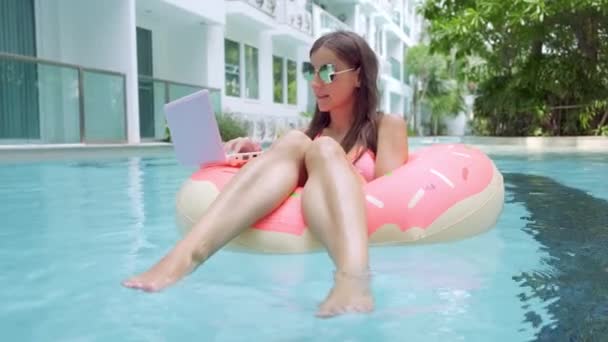 Freelance femminile si siede in un cerchio gonfiabile in piscina e lascia cadere il computer portatile in acqua. Occupato durante le vacanze. Il concetto di lavoro a distanza. focus selettivo — Video Stock