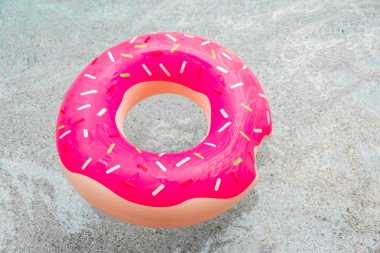 Inflatable float rubber ring in the form of a pink donut in the water of the pool clipart