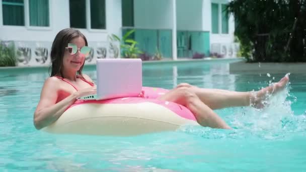 Genç kadın bir yüzme çemberinde denizde yüzerler. Kız havuzda bir bilgisayar ile şişme daire üzerinde istirahat, üst görünümü — Stok video