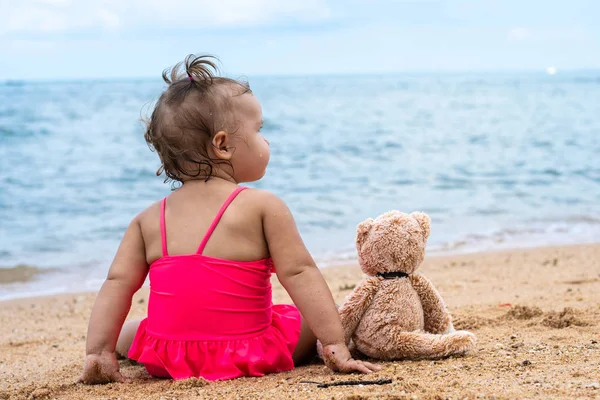 Маленькая девочка обнимает плюшевого мишку, сидящего на пляже. Не оставайся одна. Печаль и одиночество — стоковое фото