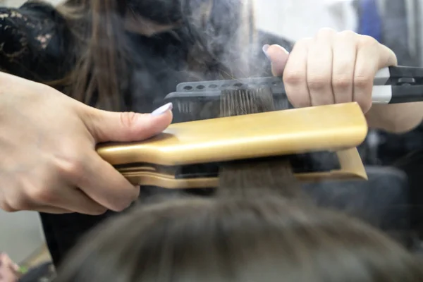 Cute girl with long brunette hair hairdresser doing hair lamination in a beauty salon. concept of hair care treatment, steam from hair