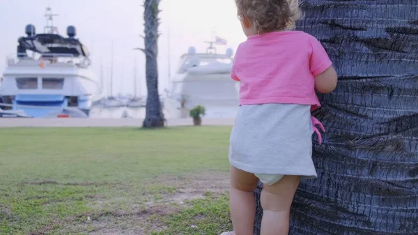 Bambina di 1 anno che corre lungo un sentiero nel parco tra palme, rallentatore, 4k . — Foto Stock