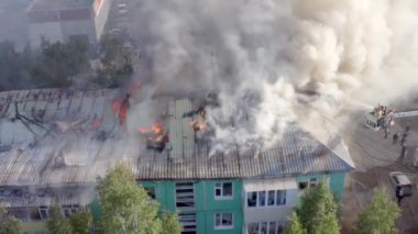 Yüksek katlı bir binanın yanan çatısı, yangından duman bulutları. İtfaiyeciler yangını söndürdü. üst görünüm