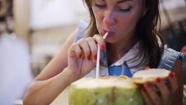 Hermosa hembra bebe coco de una paja en un café por la noche, primer plano . — Vídeo de stock