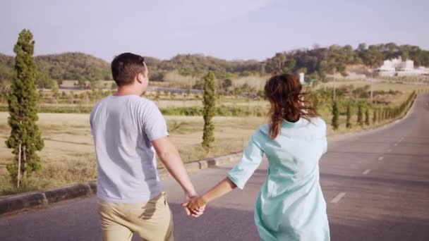 Young couple man and woman in love walking on the road among fields and mountains. Male and female strolling among fields and hills — Stock Video