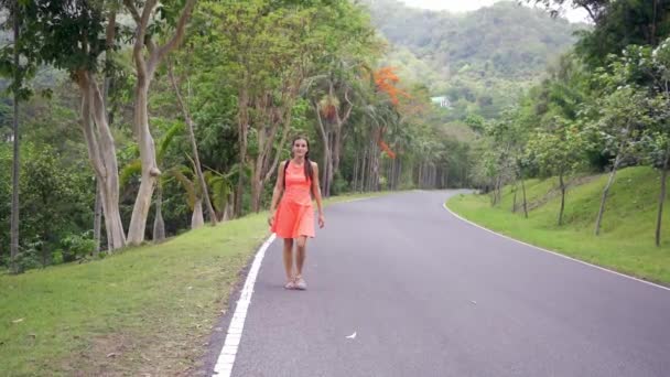 Bela floresta tropical com uma jovem viajante com uma mochila na estrada para a floresta Tailândia. Uma mulher caminha ao longo de uma estrada tropical e desfruta das vistas da natureza . — Vídeo de Stock