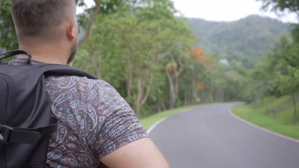 Handsome tropical forest with a traveler young man with a backpack on the road to Thailand forest. A man walks on a tropical road and enjoys the views of nature — Stock Video