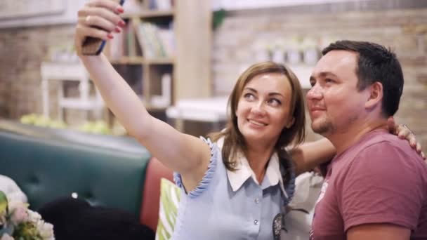 Mooi paar in de liefde zit in een café in de avond neemt een selfie foto en kusjes. — Stockvideo