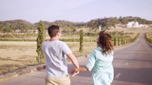 Pareja joven hombre y mujer enamorados caminando por el camino entre campos y montañas. Masculino y hembra paseando entre campos y colinas — Vídeos de Stock