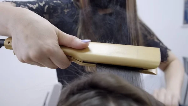 Κομμωτήριο κάνει πλαστικοποίηση και ίσιωμα των μαλλιών σε ένα σαλόνι ομορφιάς για ένα κορίτσι με καστανά μαλλιά. έννοια της φροντίδας των μαλλιών — Φωτογραφία Αρχείου