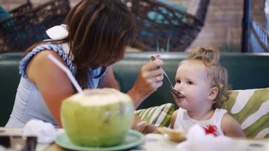 Restoranda küçük kızıyla oturan ve yemek paylaşan bir annenin portresi. Çocuklar için ilk beslenme kavramı.