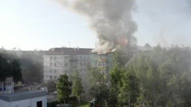 Yüksek katlı bir binanın yanan çatısı, yangından duman bulutları. İtfaiyeciler yangını söndürdü. üst görünüm