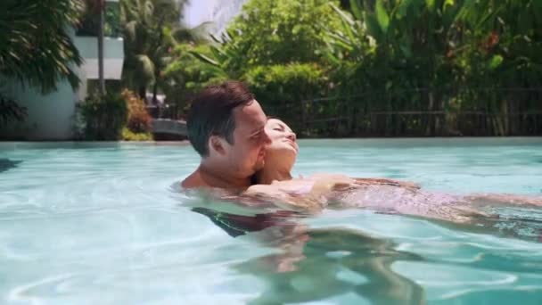 Beautiful couple in love male and female in bathing suits swim in a swimming pool in blue water. — Stock Video