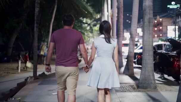 Romantische und Liebesbeziehungen. junges paar männliche und weibliche spaziergänge entlang der promenade in der nachtstraße in pattaya, thailand, rückansicht. — Stockvideo