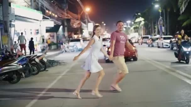 Romantiska och kärleksrelationer. Ungt par manliga och kvinnliga korsa vägen på Night Street i Pattaya, Thailand, bakifrån. — Stockvideo