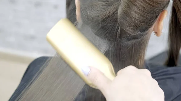 美容師は、茶色の髪を持つ女の子のための美容院でラミネートと髪の矯正を行います。ヘアケアコンセプト — ストック写真