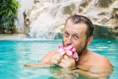 sakallı adam havuzda çiçek tutar. Tropikal çiçekler Frangipani Plumeria, Suda yüzen Leelawadee. Spa havuzu. Barış ve huzur. Spa konsepti.